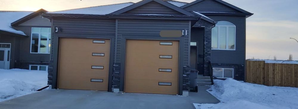 The completed Buhler Bay duplex, dark siding with timber garage doors, in winter